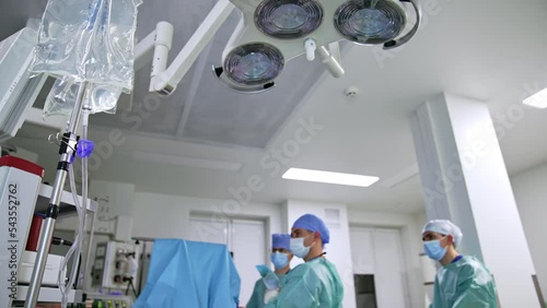 Lamp hanging from the ceiling in modern surgical room. Low angle view. Group of doctors perform operation at backdrop. photo