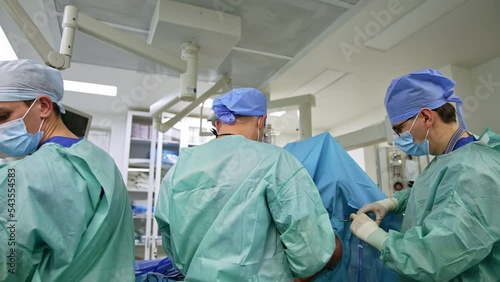 Team of surgeons in the operational room standing their backs to camera. Chief doctor sewing the patient’s shoulder at the end of surgery. photo
