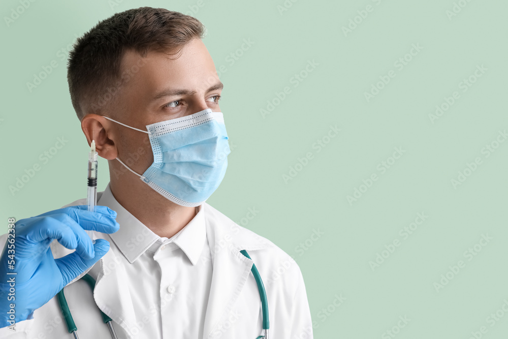 Male doctor in medical mask with syringe on green background, closeup Male doctor in medical mask with syringe on green background, closeup