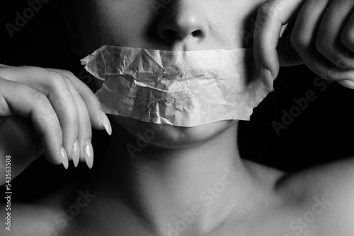 Young woman with taped mouth on dark background, closeup. Censorship concept