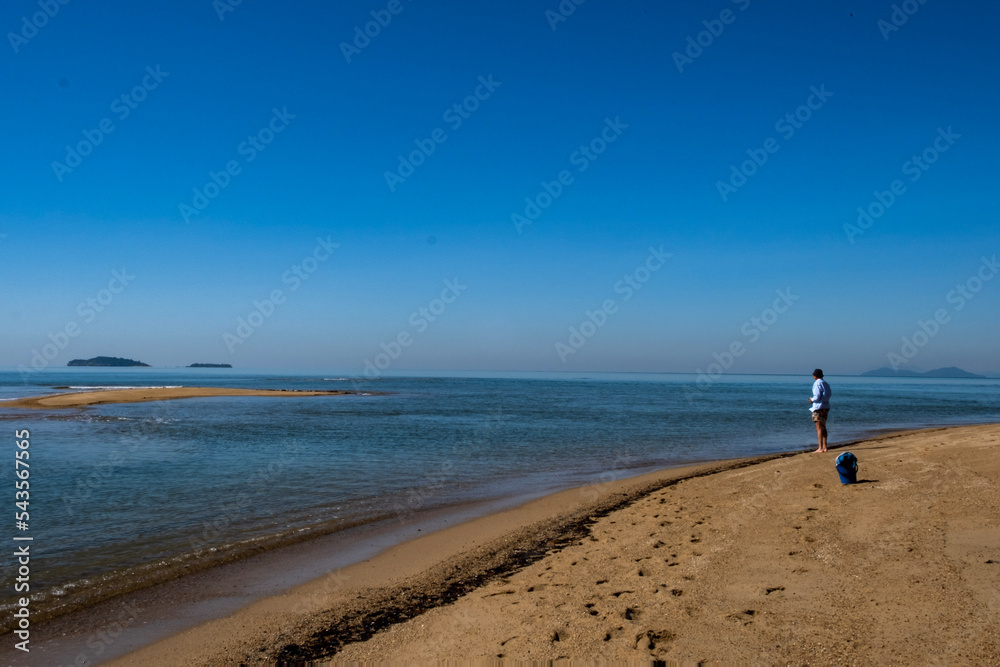 Person fishing on Cowley Beach, Cassowary Coast, Queensland, Australia. There is a vast expanse of beach, ocean and horizon