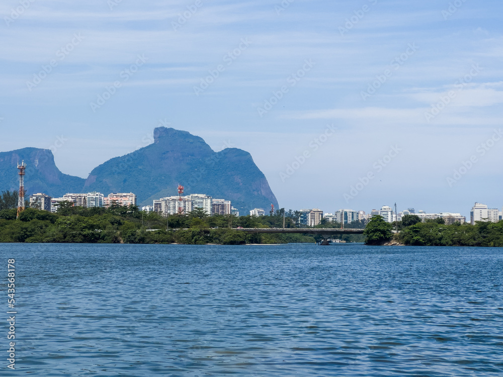 Marapendi Lagoon with buildings, vegetation and trees around. Hills and Barra da Tijuca bridge in the background. Located near Praia da Reserva in Rio de Janeiro