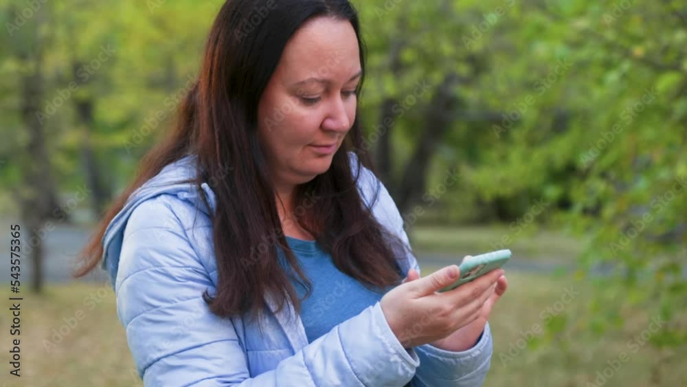 Woman using mobile phone in park. Adult female is socializing during autumn. She is spending leisure time in garden. Woman using mobile phone in park. Adult female is socializing during autumn. She is spending leisure time in garden.
