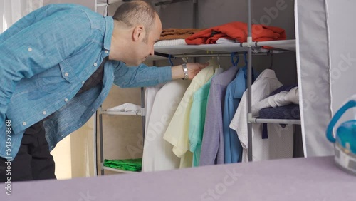 The man is choosing clothes from the closet.
Man with his clothes hanging in the closet is choosing clothes.
 photo