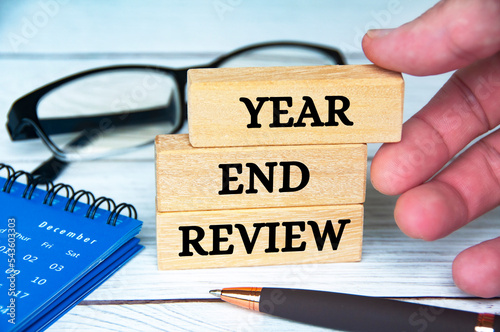 Year end review text on wooden blocks with December calendar, glasses and pen. Accounting and year end review concept.