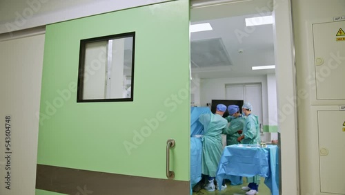 Group of surgeons in uniforms working at the operational table. Standing at the opened doors to modern surgery room photo