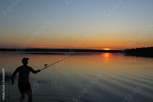 A fisherman casts a fishing rod on an evening lake at sunset