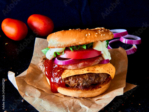 Big beef burger on baking paper with cheese full of fresh vegetable