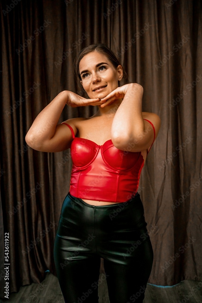Party girl portrait. Young woman in red corset and black leather pants. Sexy seductive brunette in red and black costume. Role play. Celebration and party. Having fun.