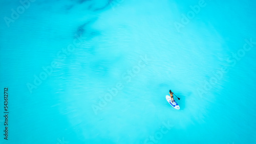 Aerial top down view of a woman on a stand up paddle (SUP) board over the turquoise Caribbean ocean in the Bahamas islands