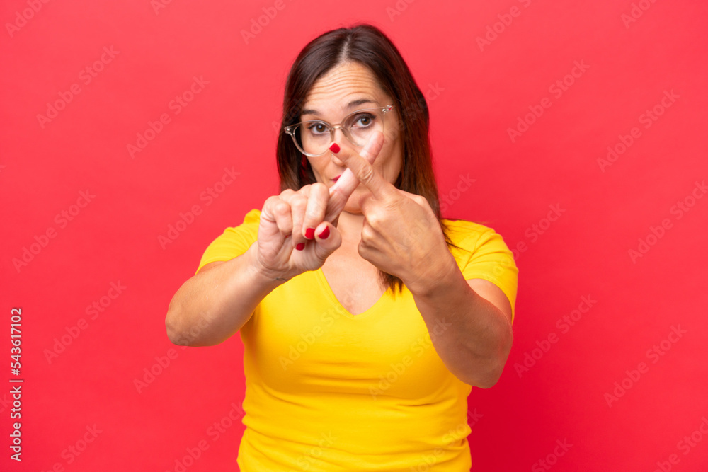 Middle-aged caucasian woman isolated on red background making stop gesture with her hand to stop an act Middle-aged caucasian woman isolated on red background making stop gesture with her hand to stop an act