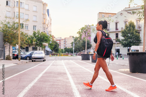 latina female athlete walking with backpack on a city running track, urban sport and healthy lifestyle concept, copy space for text