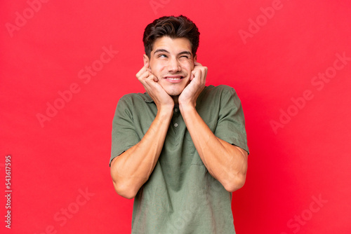 Young caucasian handsome man isolated on red background frustrated and covering ears