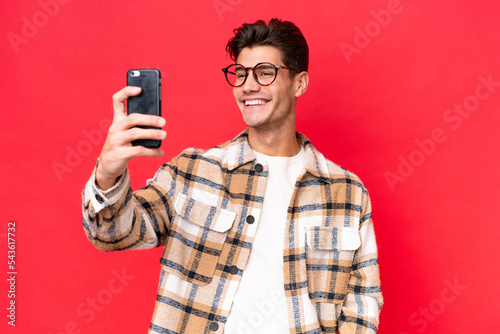 Young caucasian handsome man isolated on red background making a selfie © luismolinero