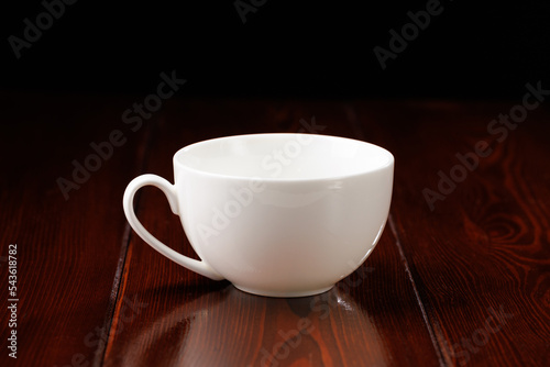 A white, clean, busty china cup against a dark wooden table. Side view.