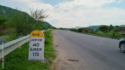 Low shot showing the milestone on national highway NH8 showing the distance to Jaipur and Ajmer as cars zoom by on this highway surrounded by mountains photo