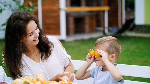summer, in the garden. a four-year-old boy, having fun with his family outdoors, twisting, applying mandarins to his eyes. family holidays, lunch on the nature, in the courtyard. High quality photo