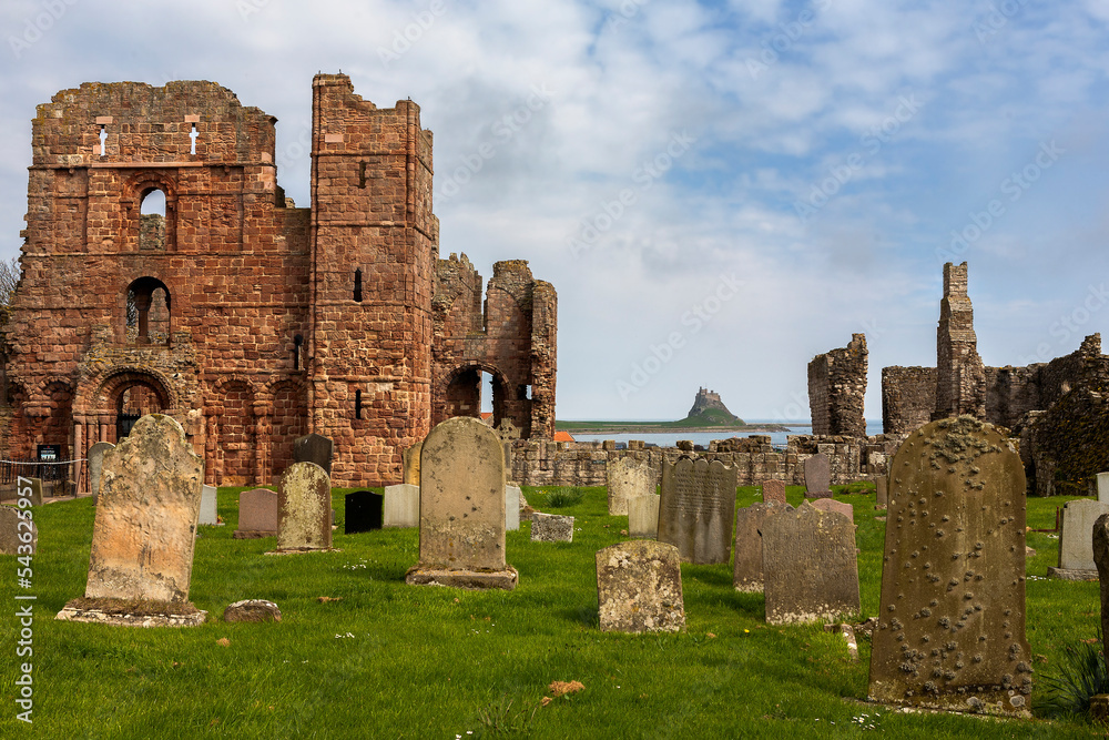 The ruins of Lindisfarne Priory and in the distance, Lindisfarne Castle, from the graveyard of the church of St. Mary the Virgin, Holy Island, Northumberland, England