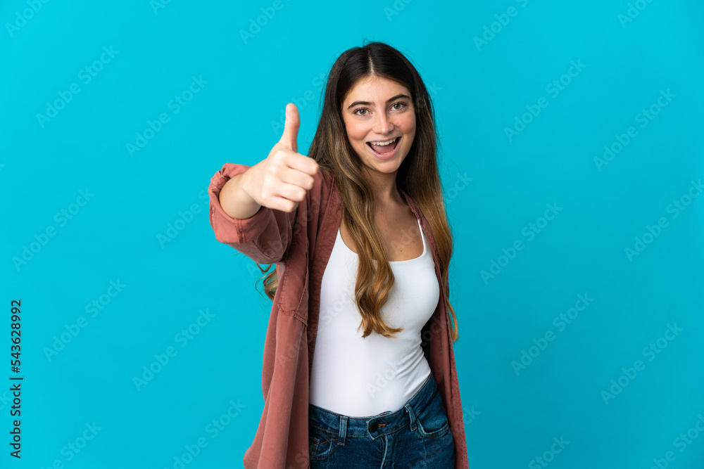 Young caucasian woman isolated on blue background with thumbs up because something good has happened
