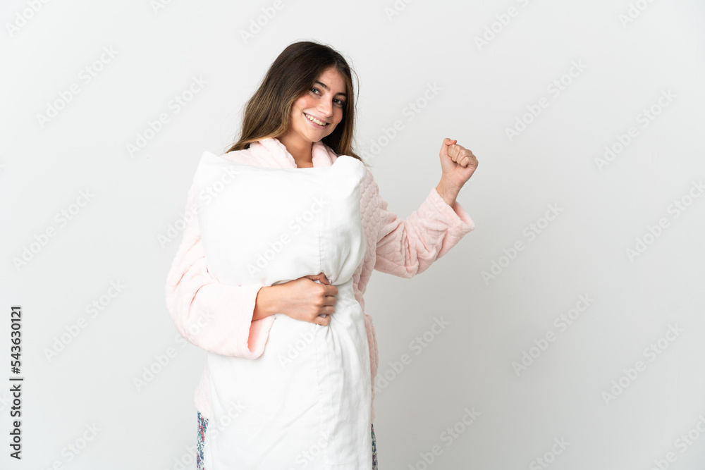 Young caucasian woman isolated on white background in pajamas and holding a pillow and celebrating a victory Young caucasian woman isolated on white background in pajamas and holding a pillow and celebrating a victory