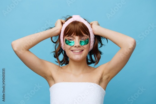 Horizontal photo, a woman with ideal smooth skin on a blue background with luxurious dark hair and bright green luxurious patches is holding her hair and is very excited