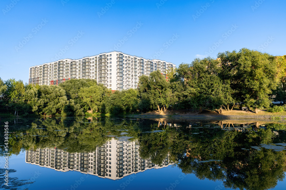 New modern residential apartment buildings near the lake surrounded by green trees and grass New modern residential apartment buildings near the lake surrounded by green trees and grass