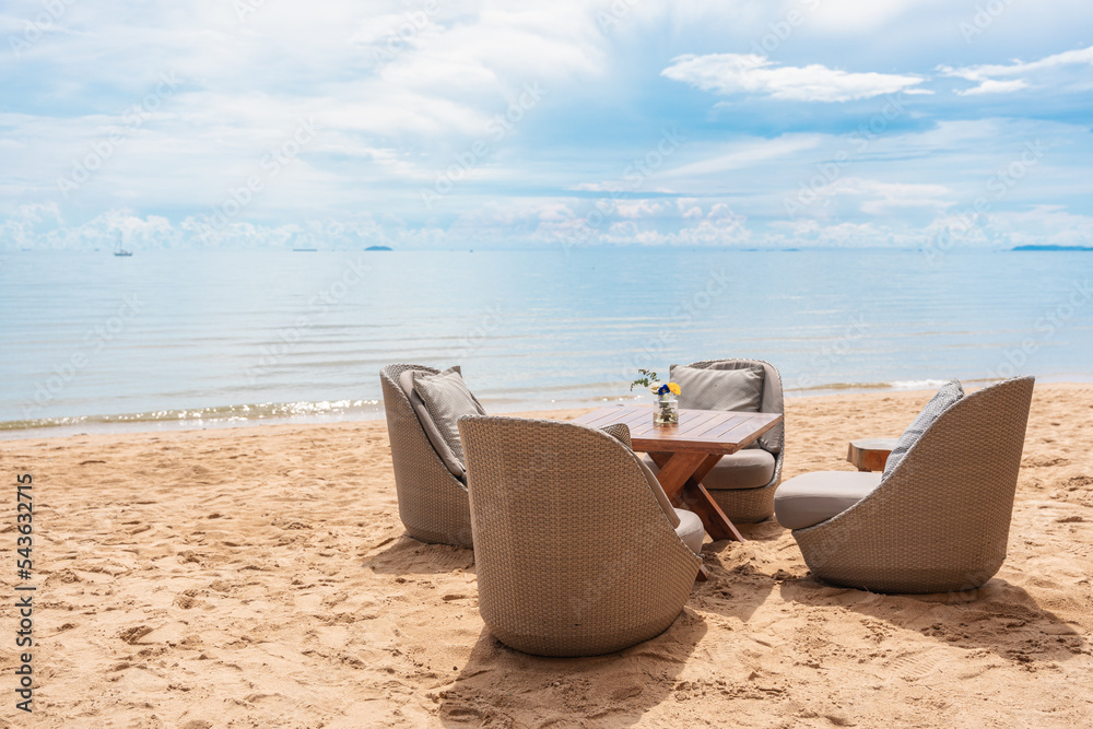 Rattan chair with pad and table setting on the beach by tropical sea Rattan chair with pad and table setting on the beach by tropical sea
