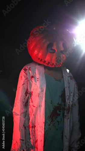 Young woman has pumpkin on her head and portrays bloodthirsty zombie with bloody clothes.