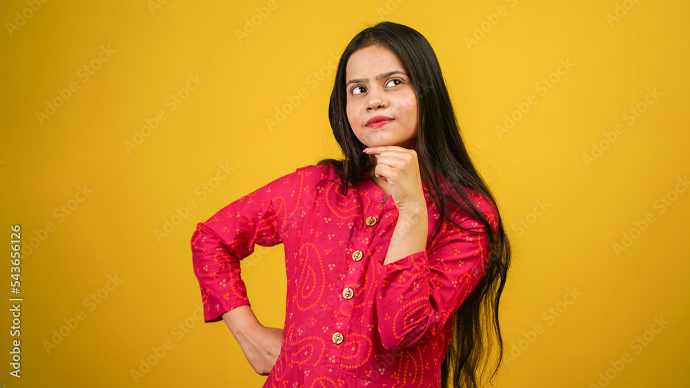 Pretty young woman looking up empty space deep thinking, holding arm on chin, isolated over yellow color background Pretty young woman looking up empty space deep thinking, holding arm on chin, isolated over yellow color background