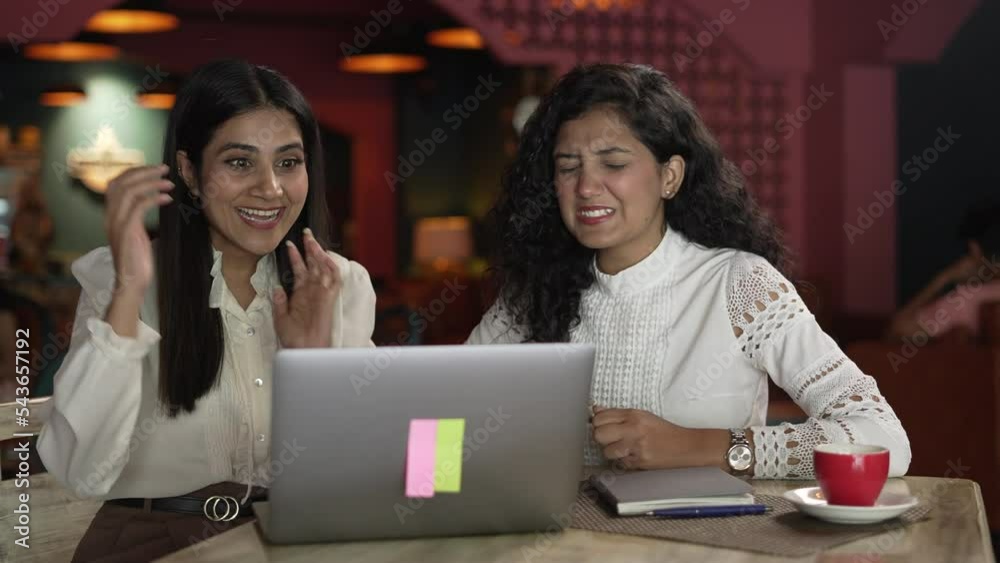 Attractive two young Asian women friends supporting different team on laptop.Indian female siting on upset with loser football game scored and other girl wining at the coffee shop.
Attractive two young Asian women friends supporting different team on laptop.Indian female siting on upset with loser football game scored and other girl wining at the coffee shop.