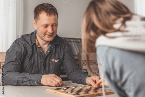 Father and daughter having fun together learning to play checkers board game at home. The concept of family leisure, communication and recreation