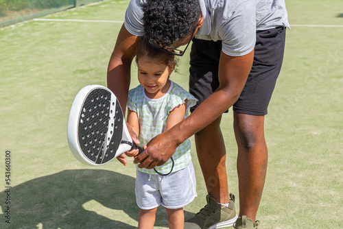 Black father teaching daughter to play paddle tennis 