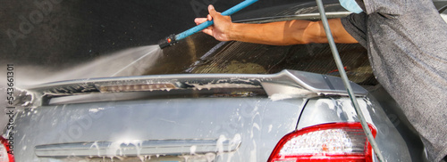 A man using washing hose washing a car in local car care shop 