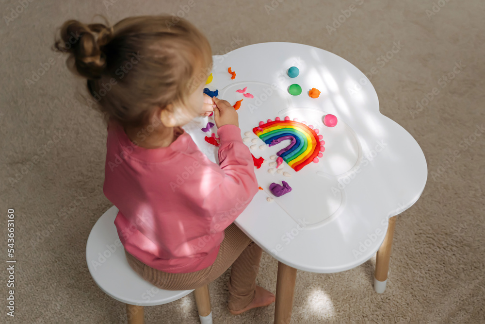 A little girl playing with rainbow from play dough for modeling. Art Activity for Kids. Fine