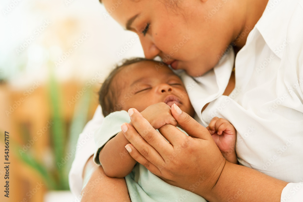 African Newborn baby one-month-old holding fingers mother's hand, sleep relax worry-free in warm embrace mom. image with a shallow depth of field, Select focus area hand. concept family mixed race. African Newborn baby one-month-old holding fingers mother's hand, sleep relax worry-free in warm embrace mom. image with a shallow depth of field, Select focus area hand. concept family mixed race.