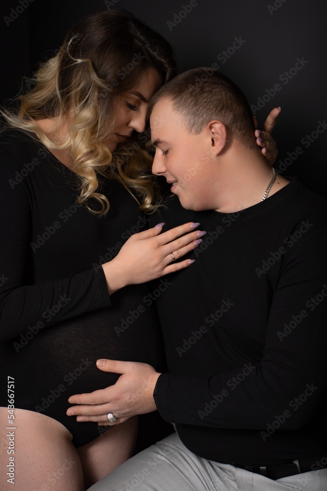 pregnant woman in a black bodysuit and a man on a black background. Long curly hair, beautiful couple, husband and wife, future parents. stylish pregnancy. portrait pregnant woman in a black bodysuit and a man on a black background. Long curly hair, beautiful couple, husband and wife, future parents. stylish pregnancy. portrait