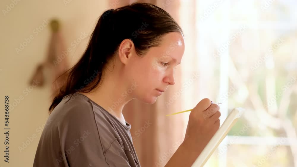 Closeup talented woman painter working on easel with paint tools. Focused girl painting picture outdoor. Portrait of thoughtful long hair artist creating artwork on nature windy day. Art concept Closeup talented woman painter working on easel with paint tools. Focused girl painting picture outdoor. Portrait of thoughtful long hair artist creating artwork on nature windy day. Art concept