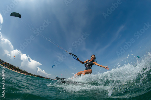 Female Kite surfer riding a kiteboard on the sea with splash.