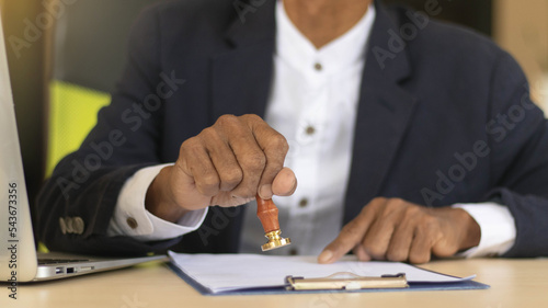 Business man person's hand stamping with approved stamp on certificate document public paper at desk, signing on business partner paper to success, or concept of attorney and insurance