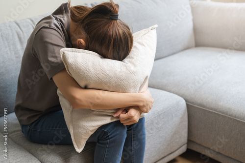 Mental health, depressed sad asian young woman, girl sitting on sofa or couch, cover face with pillow. Difficulty, failure and exhausted. Thoughtful worried suffering depression feeling alone at home.