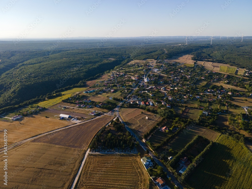 Areal shot of forests with wind turbine in the background of a small villiage and fields