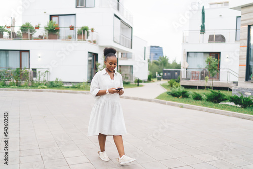 Stylish black female walking on street with smartphone