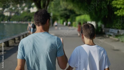 Parent giving life advice to teenager kid. Back of father and son walking together outside in park city. Dad talking to boy. manhood concept
