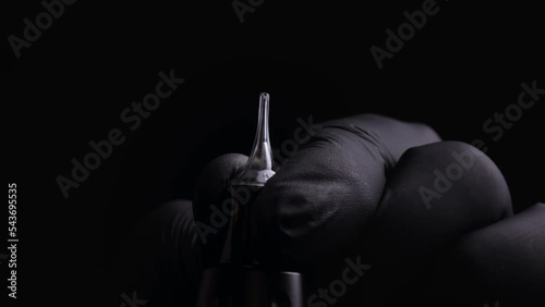 Hands of a master of permanent make-up of eyebrows, lips and eyelashes in black sterile gloves. With macro shot of installing a cartridge for permanent makeup in a tattoo machine and snapping the lock