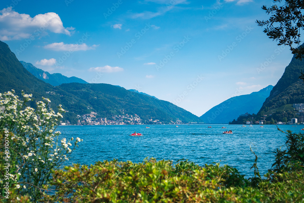 Stunning landscape of picturesque Lake Lugano and the green lush Swiss Alps in the distance. Idyllic town Lugano, Switzerland, on a sunny summer day.