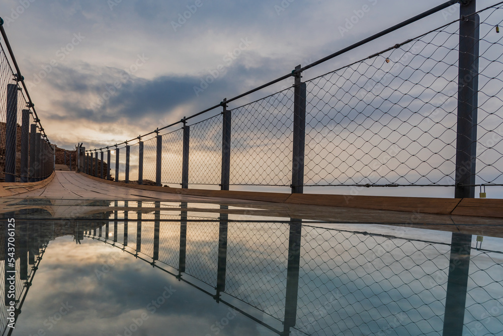 Obraz premium Jolucar suspension walkway, in Torrenueva Costa, Granada, view of the glass floor with the cloudy sky at dawn reflected on the glass.