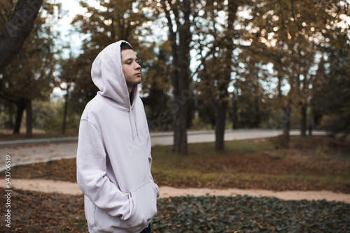 Young depressed teenager boy 22-24 year old wear hoodie with hood in dark over nature background outdoor. Lonely teen man abandoned. photo