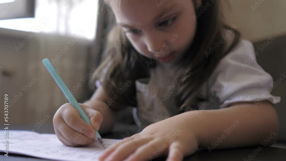 Cute smart preschool 5 years old girl writing homework in exercise copybook, learning letters, sitting at home table. Preparation for school. Home distance education. Children preschool concept. Cute smart preschool 5 years old girl writing homework in exercise copybook, learning letters, sitting at home table. Preparation for school. Home distance education. Children preschool concept.