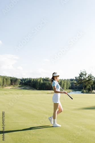 Woman in stylish summer golf outfit walking on beautiful green course for golf game. High quality photo