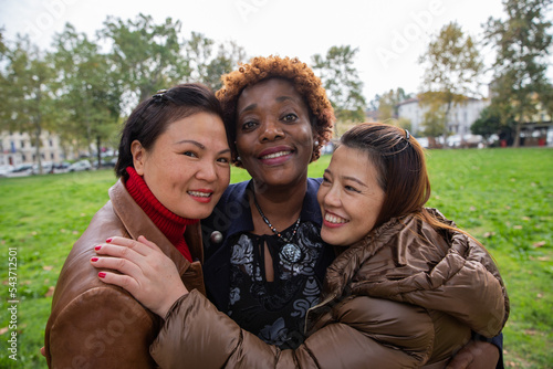 Three multiracial smiling female friends embraced during a walk at the city park